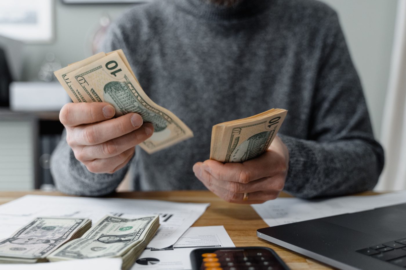 Person at a desk counting cash payments next to bills and a calculator, representing scheduled loan repayments